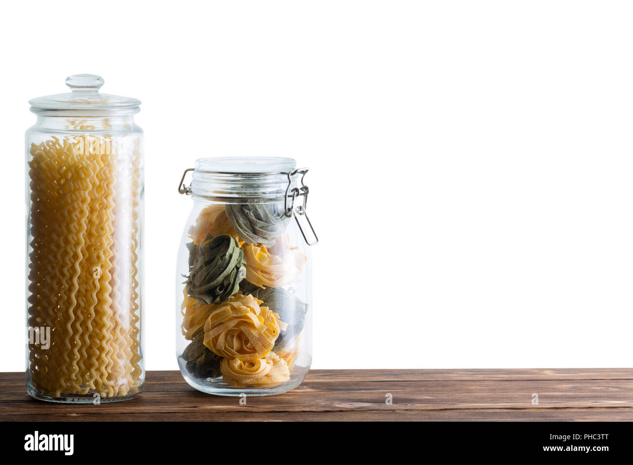 Due storage vasi riempiti con freschi di pasta essiccata con fettuccine fatte in casa e fusilli bucati lunghi lungo spirali contro uno sfondo bianco con copia s Foto Stock