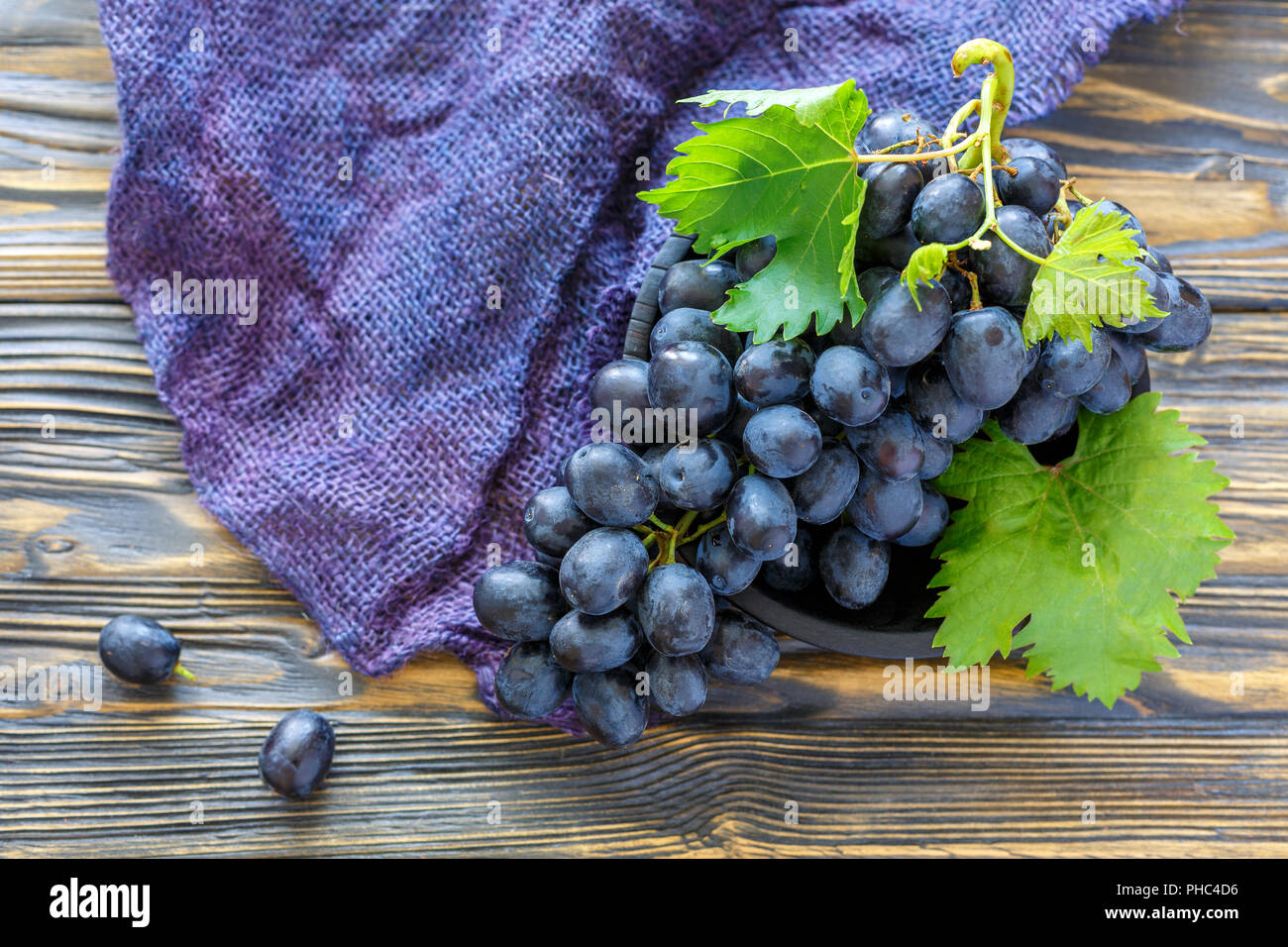 Grappolo di uva nera in una vecchia ciotola di legno. Foto Stock