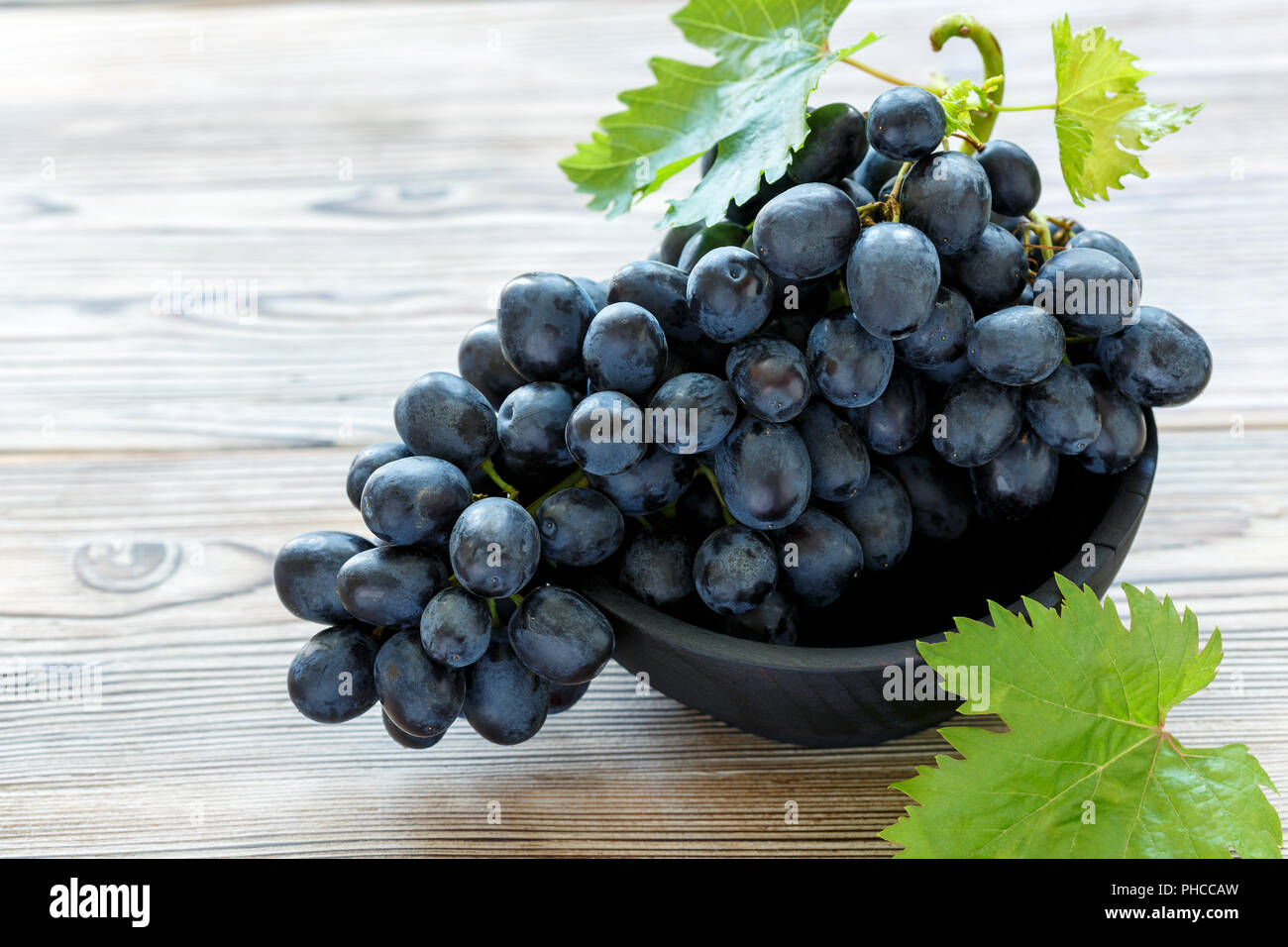 Grappolo di uva nera in una ciotola di legno. Foto Stock