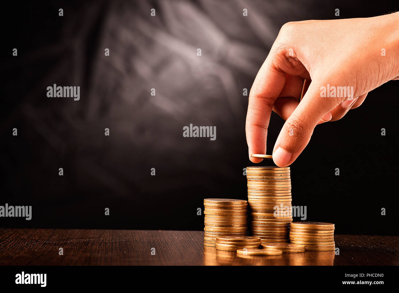 Mettendo mano monete sulle monete pila sgaint sfondo scuro, investimenti, bancario, salvataggio, finanza, crescita, passivo, reddito, interesse, concetto di stipendio. Foto Stock