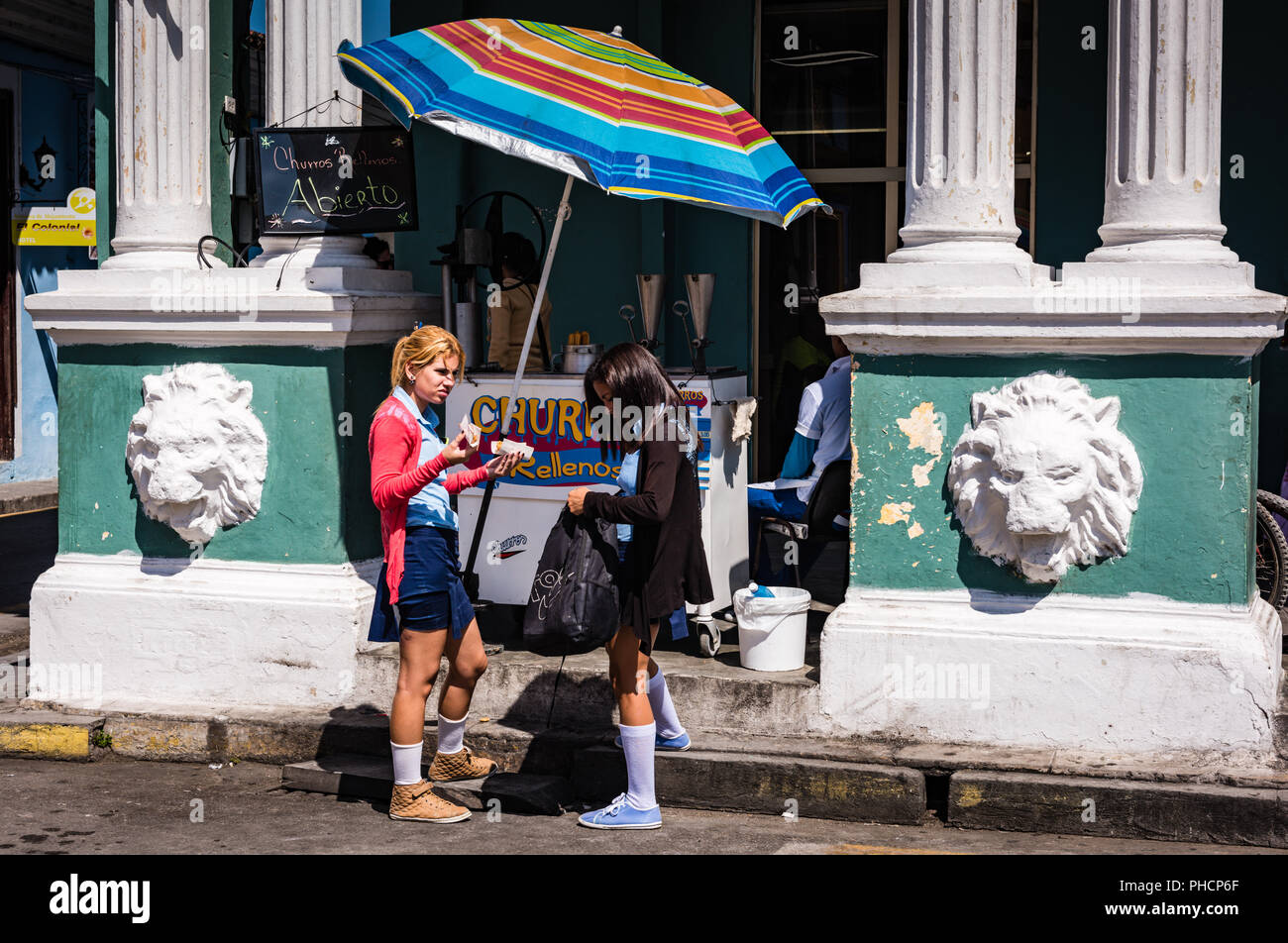 Sancti Spiritus , Cuba / Marzo 15, 2017: uniformata studentesse cubano acquistare spuntini in un riempito churro sostare davanti a un edificio fatiscente in Foto Stock