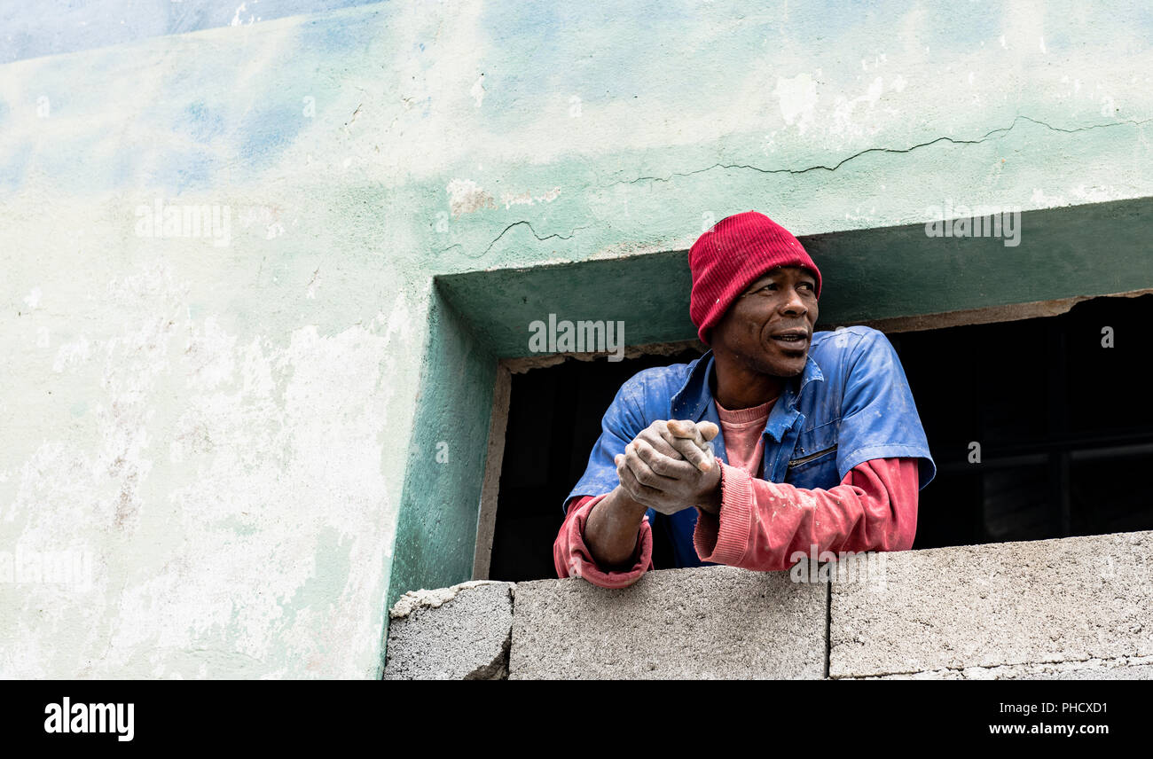 Costruzione cubano lavoratore si prende una pausa per il peer fuori dalla finestra nella Vecchia Havana, Cuba. Foto Stock