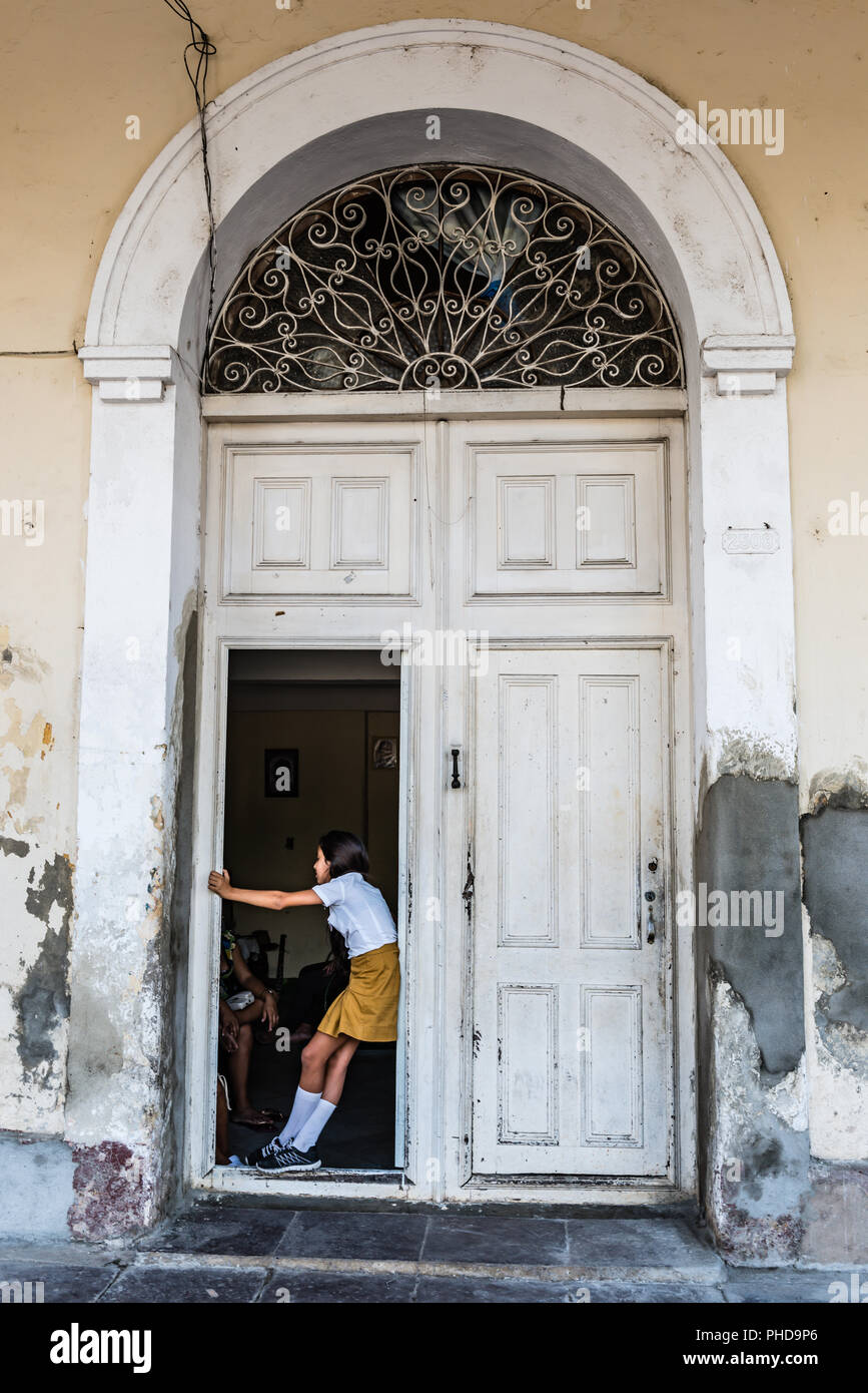 Cienfuegos, Cuba / Marzo 15, 2016: Ragazza in uniforme scolastica permanente al porta aperta di indossato alto portale ad arco. Foto Stock