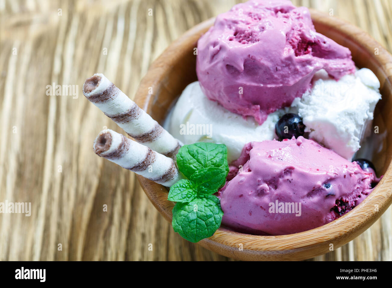 Vanilno-berry gelato con rotoli di wafer in una ciotola di legno. Foto Stock