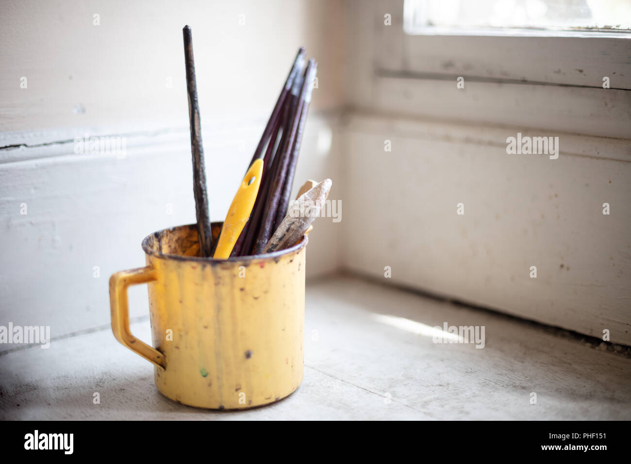 Piccolo secchio di plastica con utilizzato artista pennelli per dipingere su una mensola ad angolo al di sotto di una finestra Foto Stock