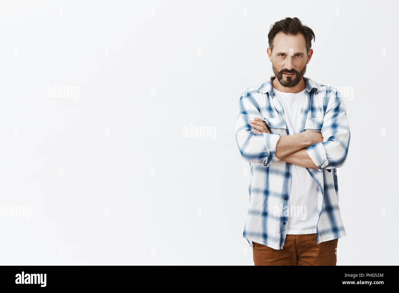 Guy sensazione disprezzo, chiusura stesso da persone in piedi in difesa posano con mani incrociate sul petto e guardando con odio e rabbia da sotto di fronte alla telecamera, che esprimono disprezzo oltre il muro grigio Foto Stock