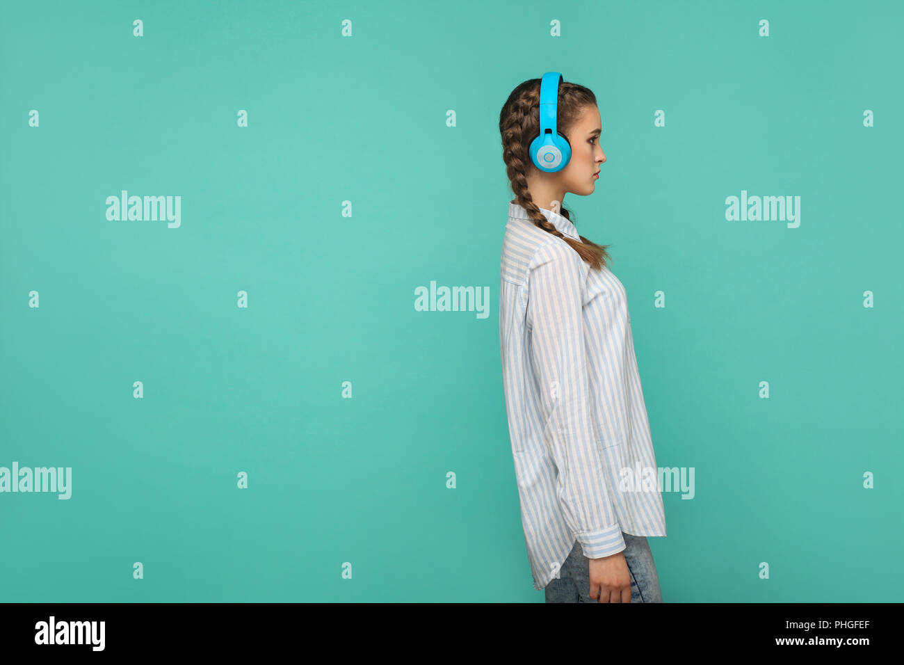 Profilo vista laterale della ragazza in striped maglietta blu e la spiralina acconciatura, piedi ascoltando musica con le cuffie e guardando lontano con faccia grave, Ind Foto Stock