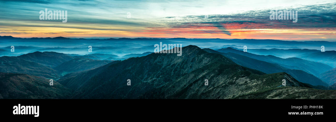 Panorama con montagne blu e colline al tramonto Foto Stock