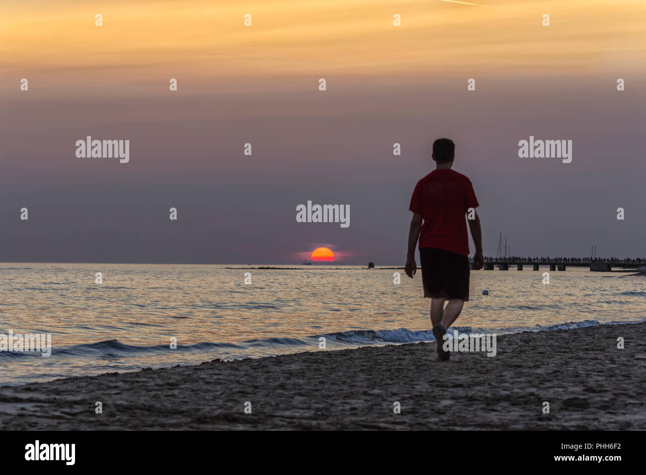 Giovane uomo per passeggiare sulla spiaggia verso il tramonto Foto Stock