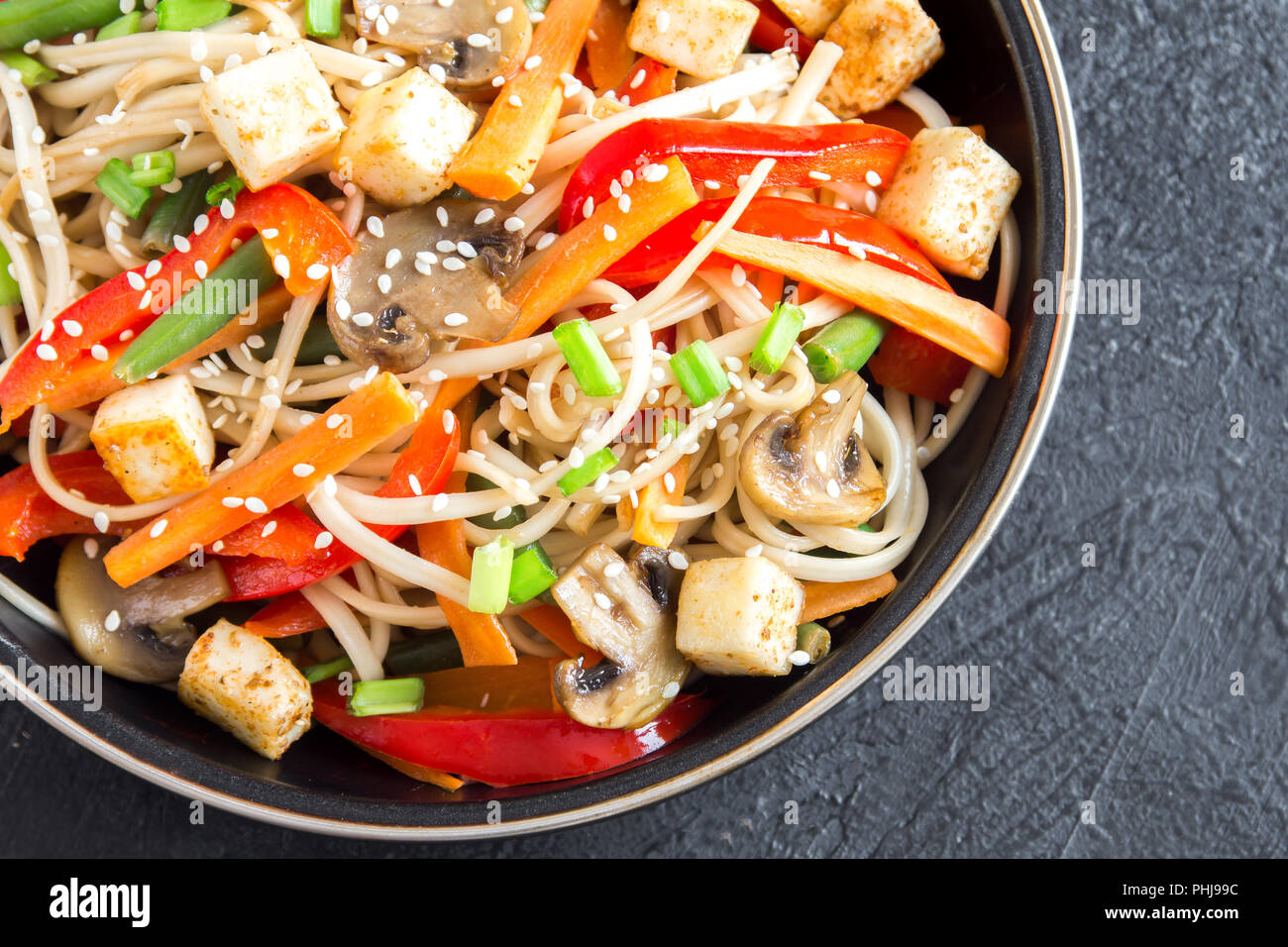 Stir fry con udon noodles, tofu, funghi e ortaggi. Asian vegane cibo vegetariano, pasto, friggere nel wok su sfondo nero, copia dello spazio. Foto Stock