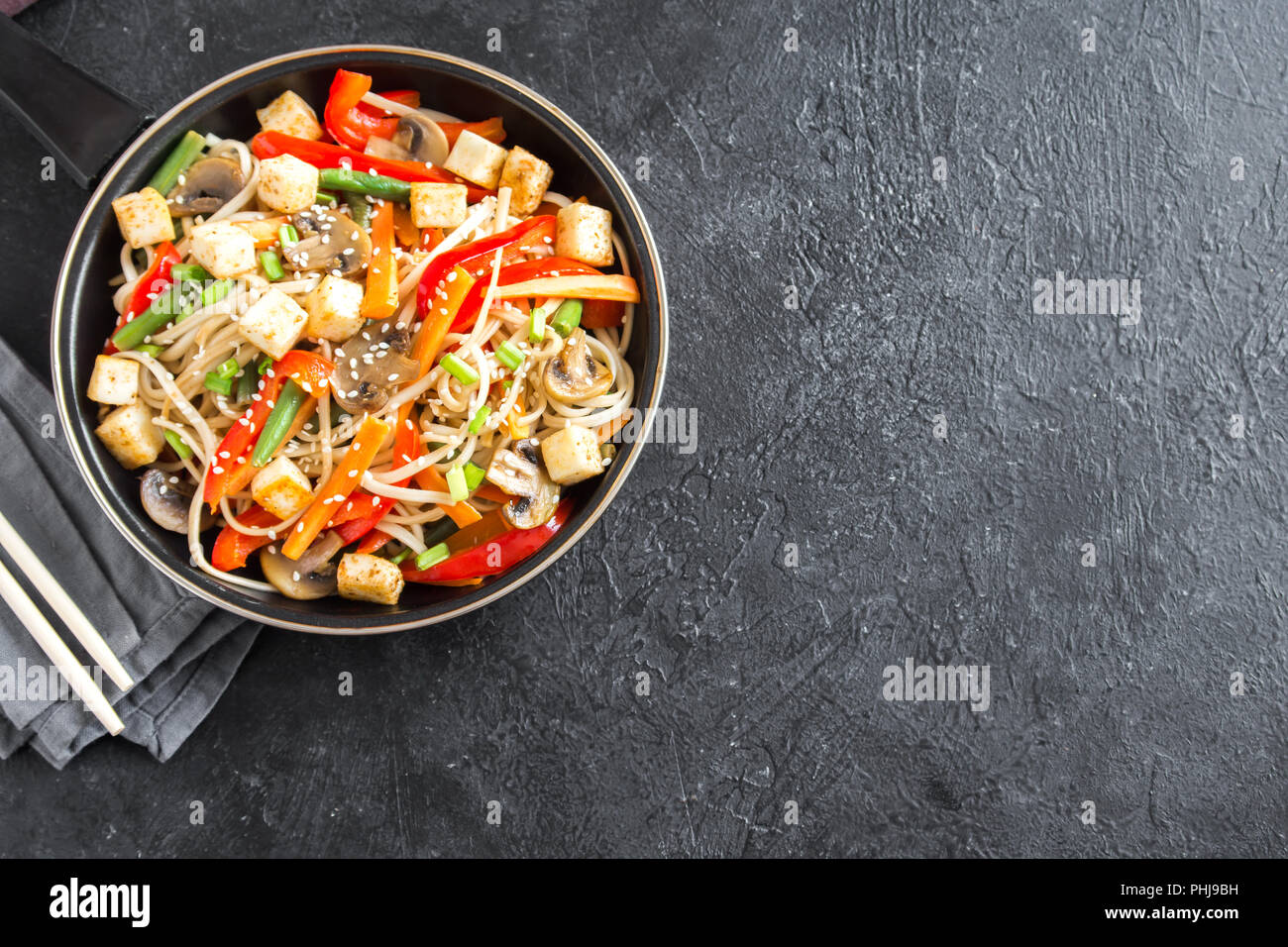 Stir fry con udon noodles, tofu, funghi e ortaggi. Asian vegane cibo vegetariano, pasto, friggere nel wok su sfondo nero, copia dello spazio. Foto Stock