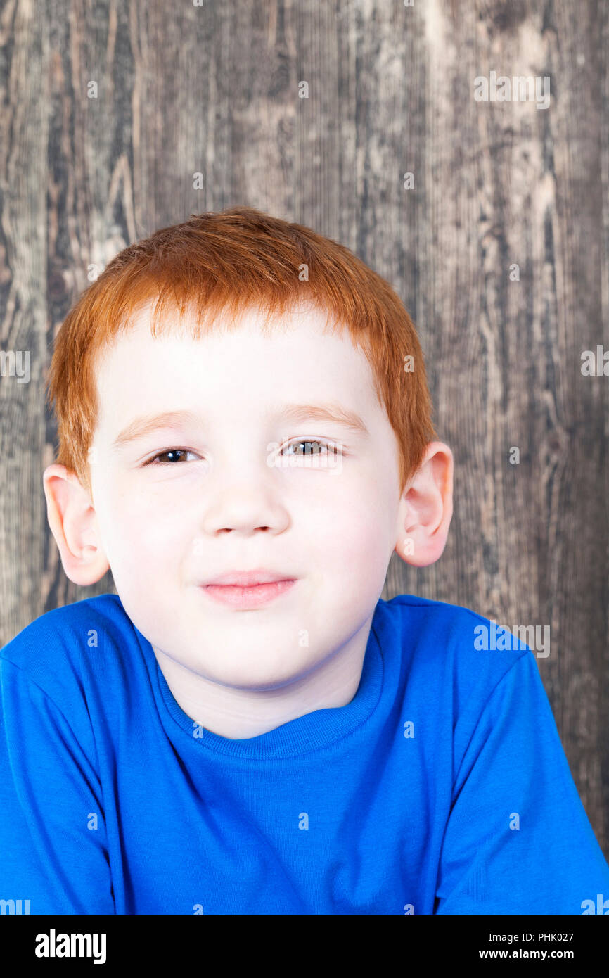 Astuzia aspetto di un i capelli rossi boy in un serbatoio blu in cima contro un nero tavola di legno, closeup ritratto Foto Stock
