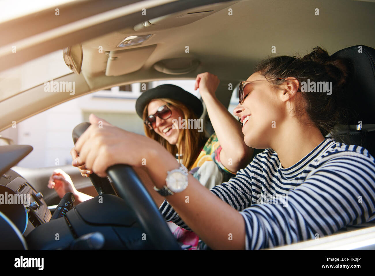 Due eleganti e attraenti le giovani donne che indossano occhiali da sole cantando la musica durante la guida di una vettura insieme in un viaggio su strada Foto Stock