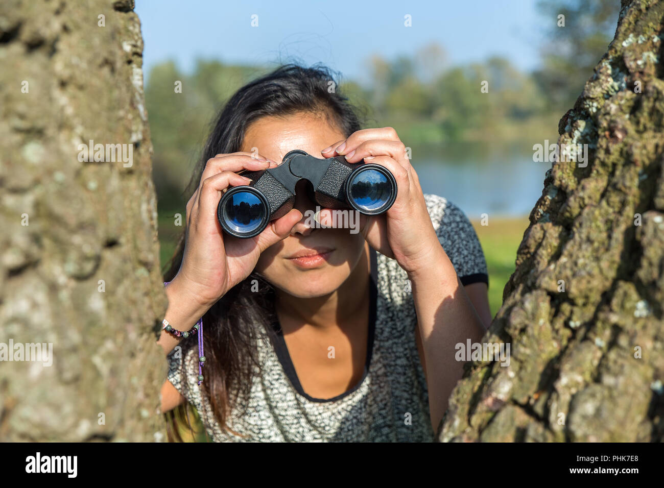 Donna che guarda attraverso il binocolo nei pressi di alberi Foto Stock