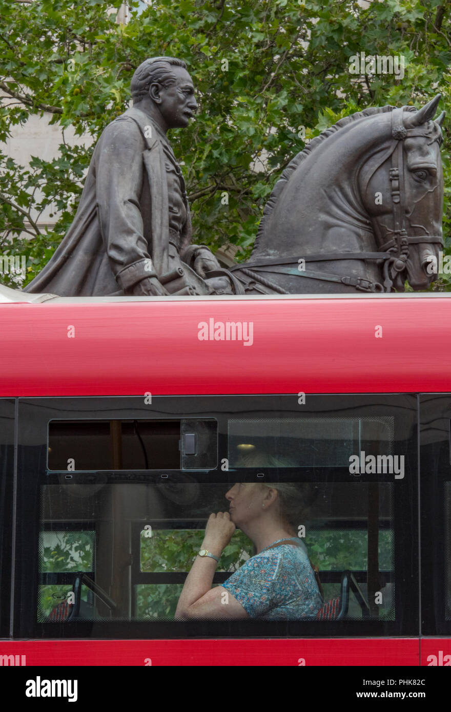 Uomo seduto sul ponte superiore di una tradizionale rosso lonon double-decker bus con montato un cavaliere statua dietro o in background. divertente immagine. Foto Stock