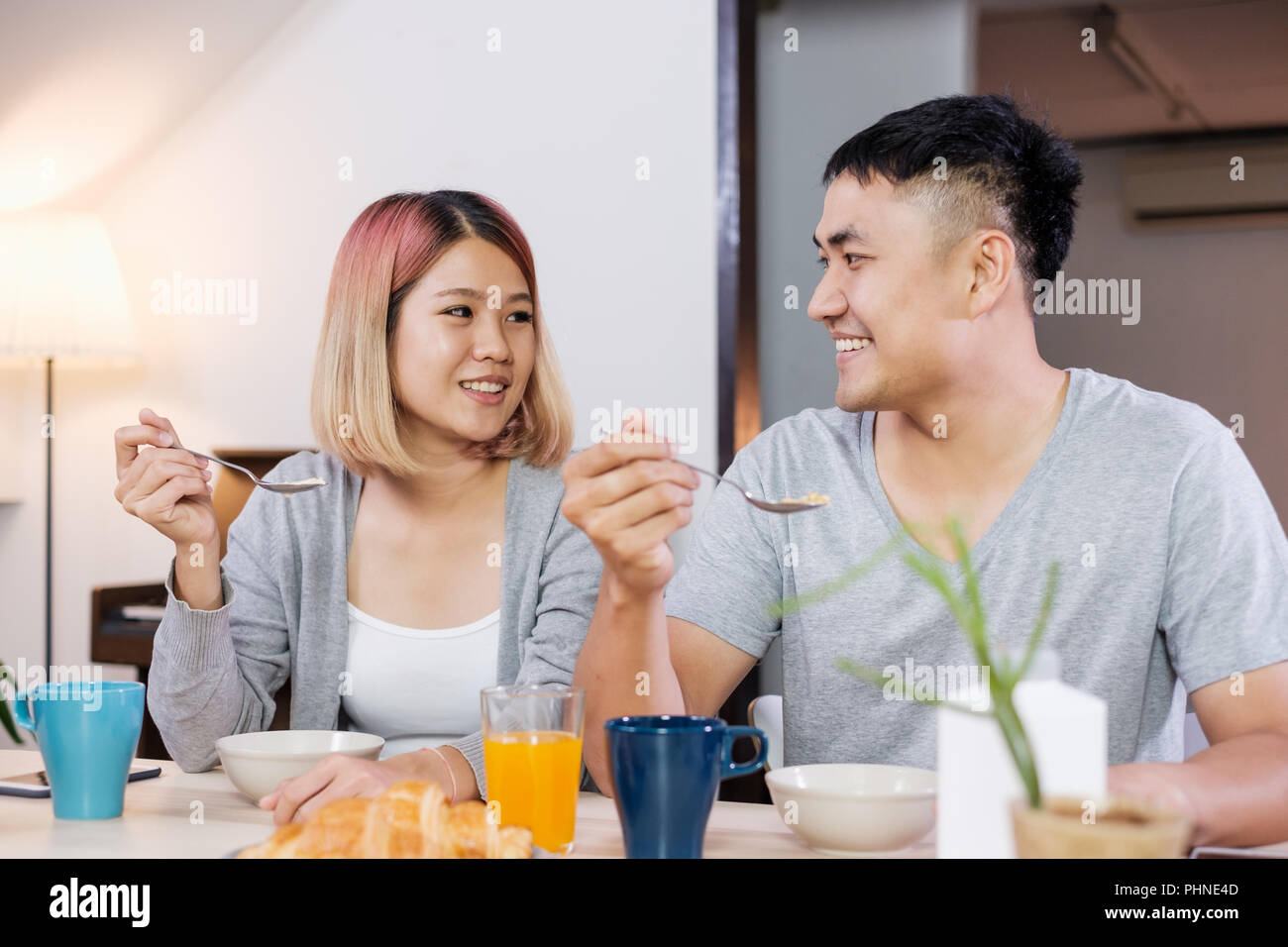 Felice coppia asiatica in pigiama seduta a tavola in cucina a casa la mattina e avente cereale colazione insieme Foto Stock