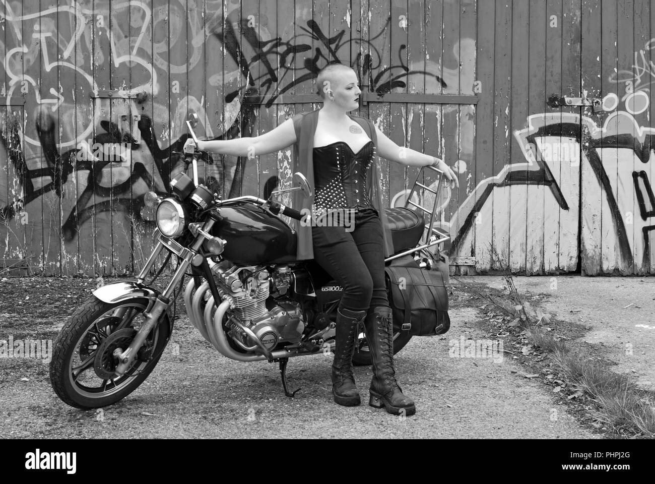 Rosa Fury seduto su una Suzuki Motorcycle, fatto cenno . Sta indossando un corto abito nero perizoma e calze e ha un casco del motociclo di fronte a lei Foto Stock