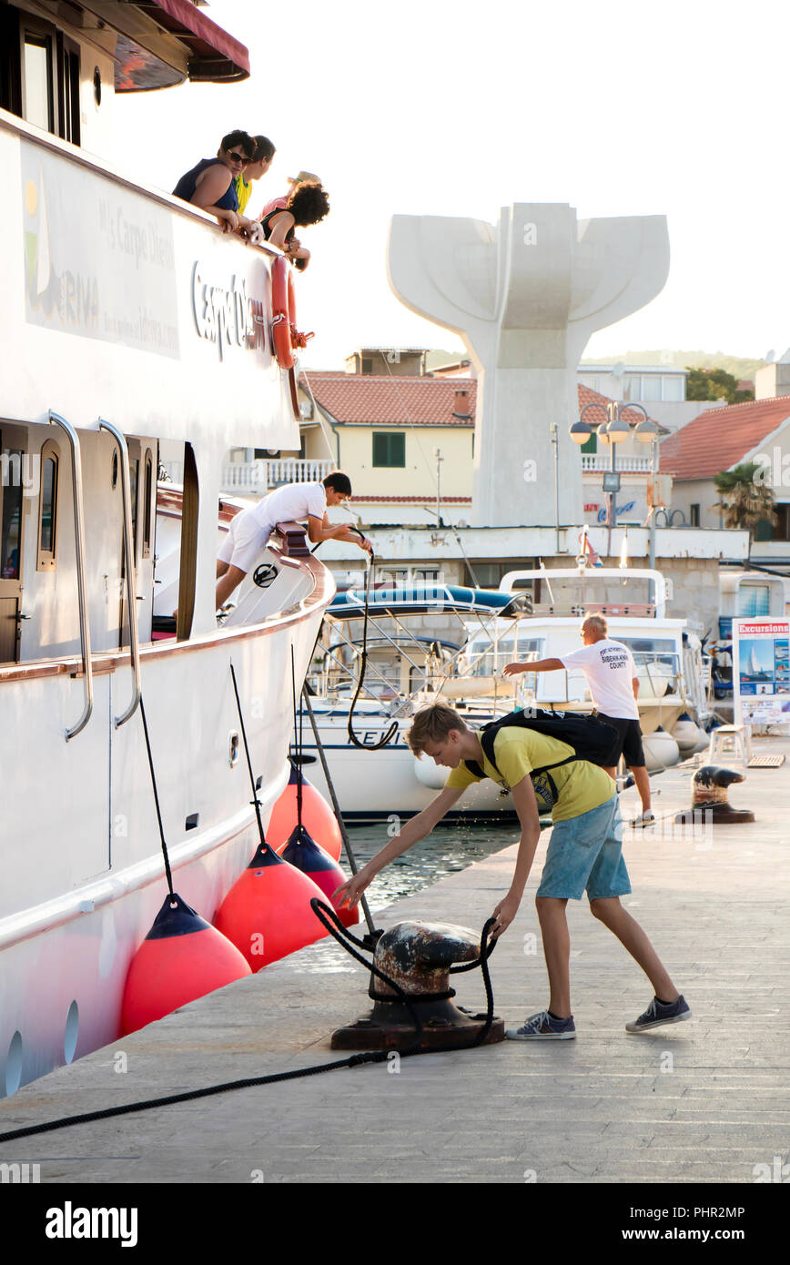 Vodice Croazia - Agosto 11, 2018: una nave da crociera di Carpe Diem arrivando a Vodice e docking. Un uomo e un ragazzo adolescente su un molo il fissaggio della corda di nave Foto Stock