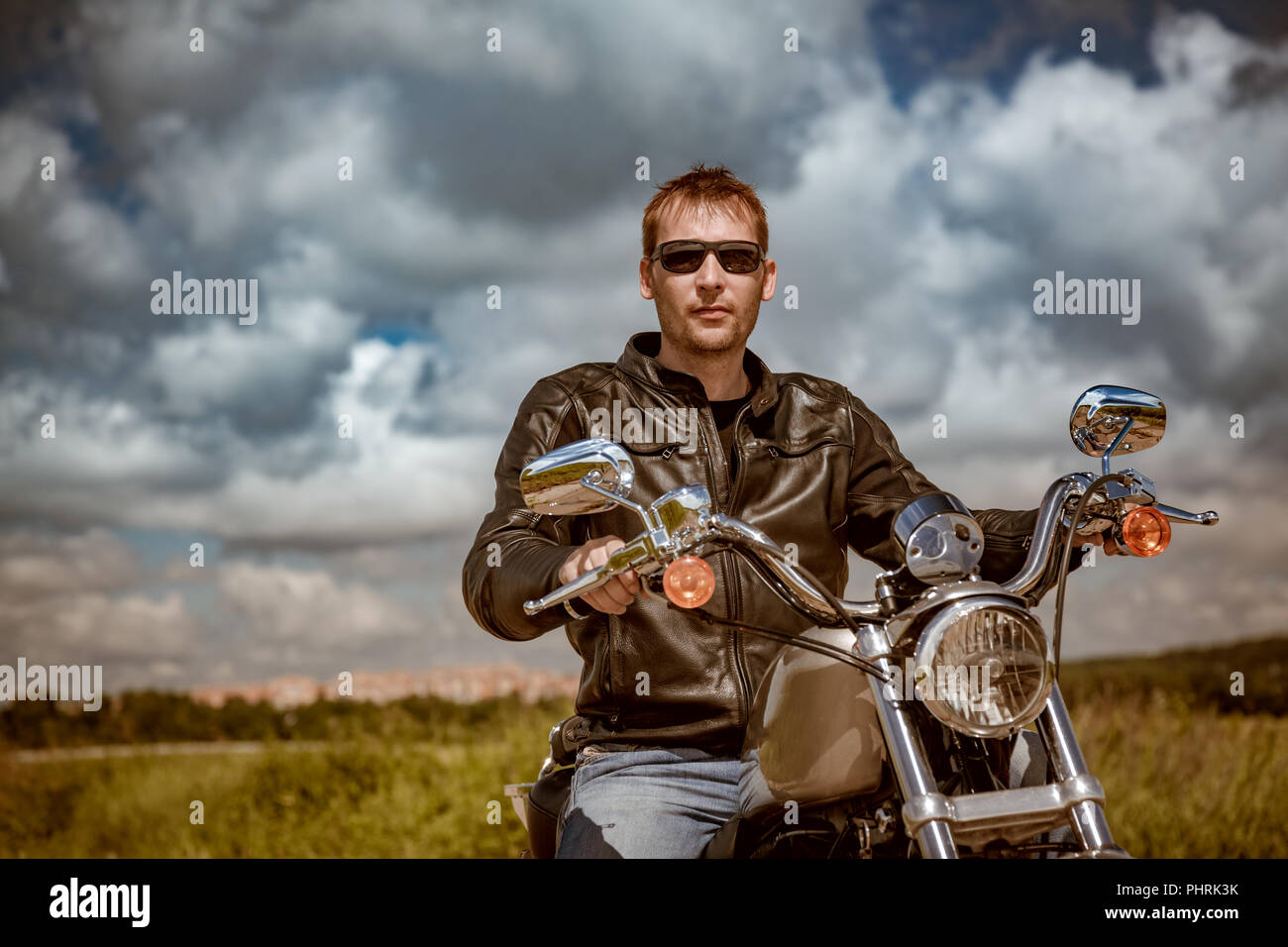 Biker uomo che indossa una giacca di pelle e occhiali da sole seduto su una motocicletta Foto Stock