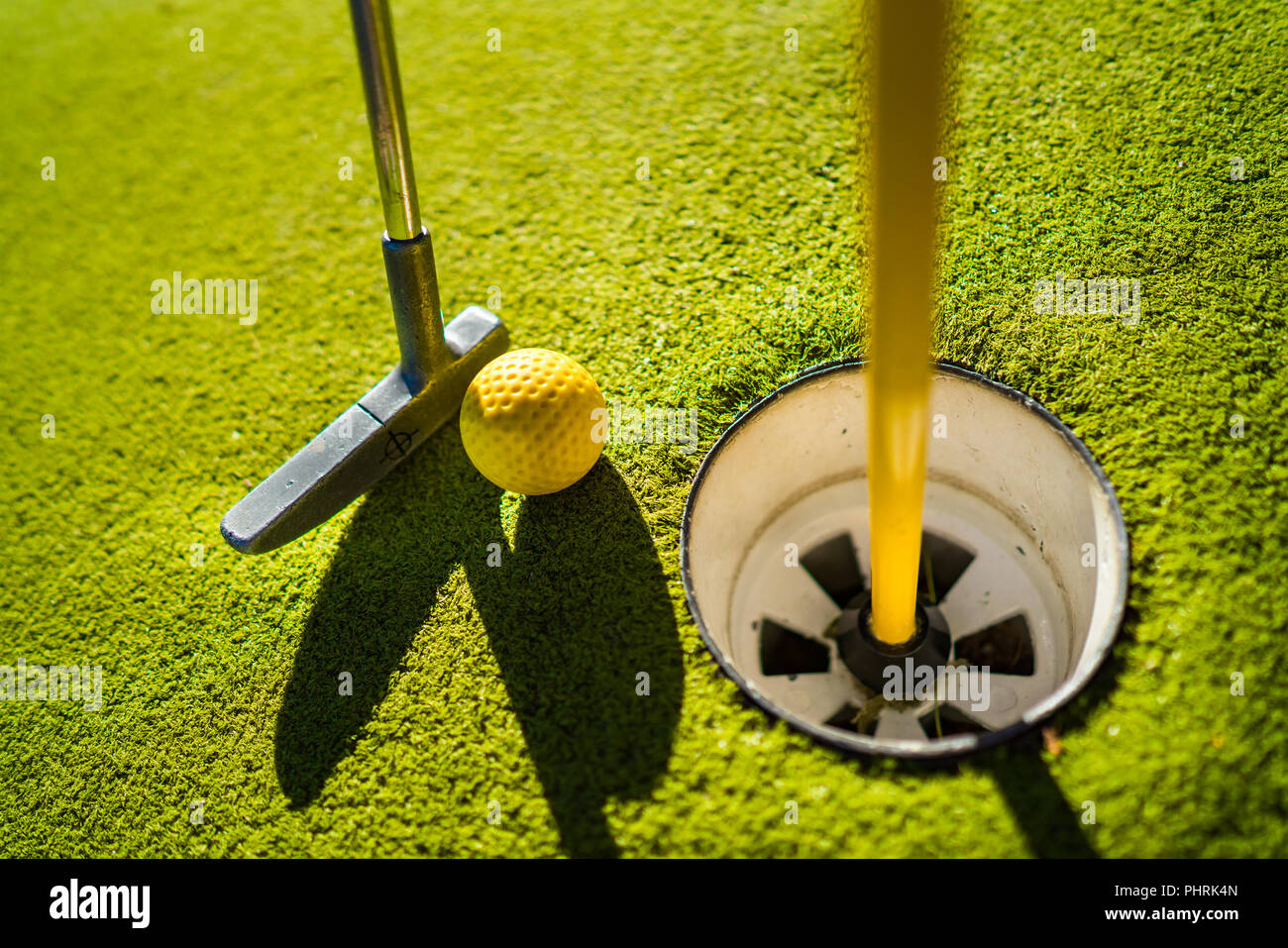 Mini Golf sfera gialla con un bat in prossimità del foro al tramonto Foto Stock