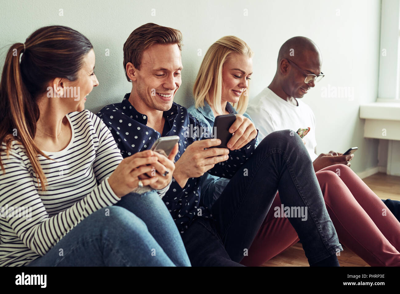 Gruppo di diversi giovani imprenditori seduti insieme su un pavimento di Office utilizzando i loro telefoni cellulari durante l'aperitivo Foto Stock