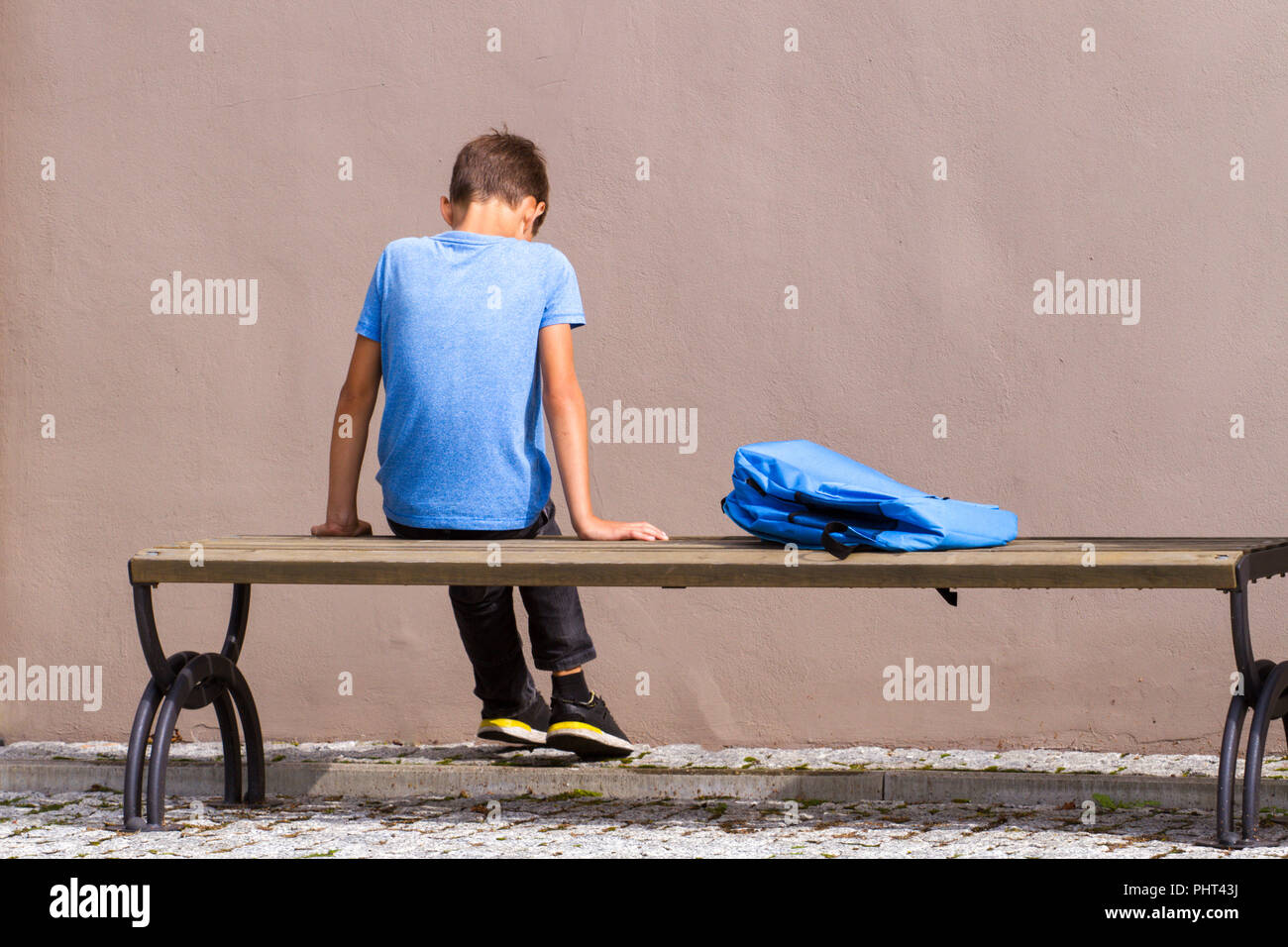 Triste, stanco bambino seduto da solo sul banco di prova all'esterno. Foto Stock