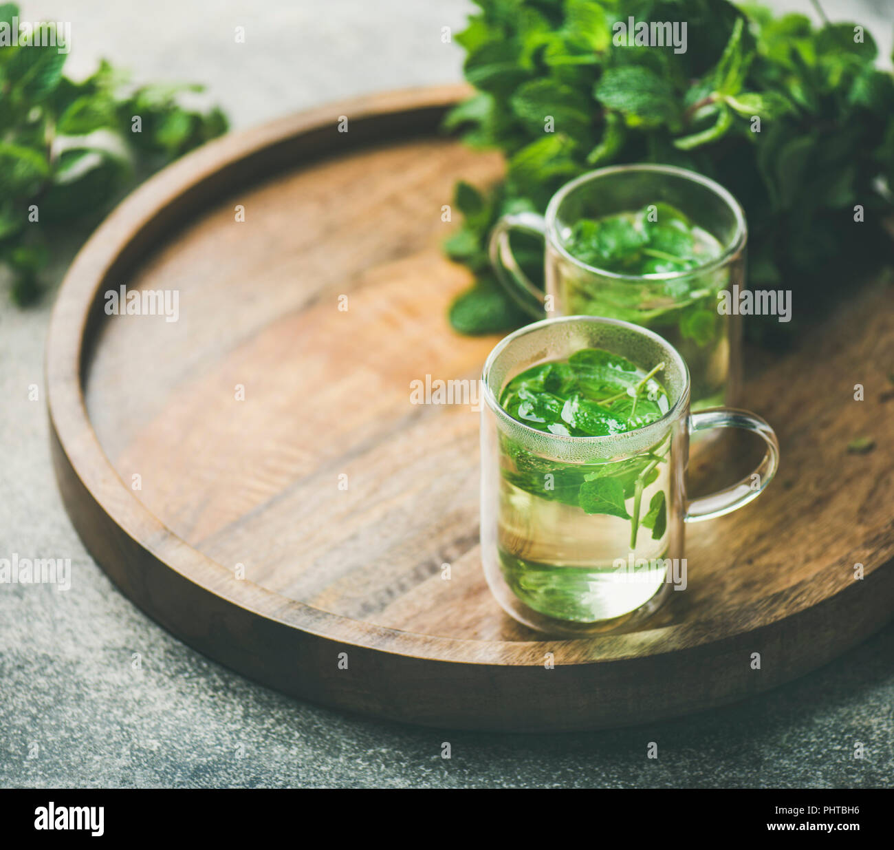 A base di erbe calde tè alla menta bevande in bicchieri di vetro sopra il vassoio in legno con fresco giardino con foglie di menta, il fuoco selettivo, copia dello spazio, composizione orizzontale Foto Stock