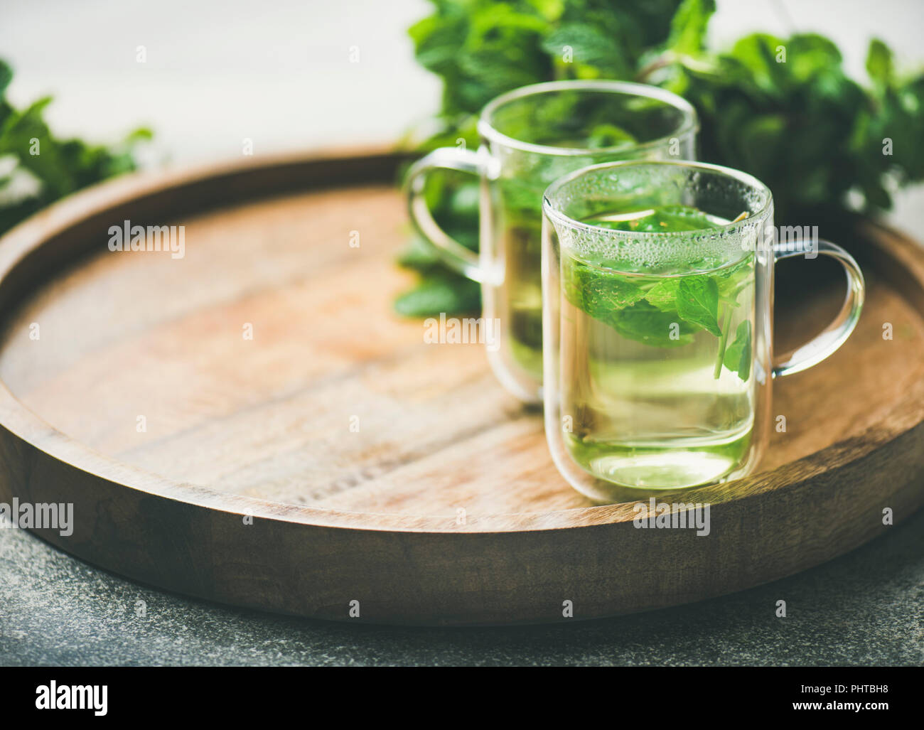 A base di erbe calde tè alla menta bevande in bicchieri di vetro sopra il vassoio in legno con fresco giardino con foglie di menta, il fuoco selettivo, spazio di copia Foto Stock