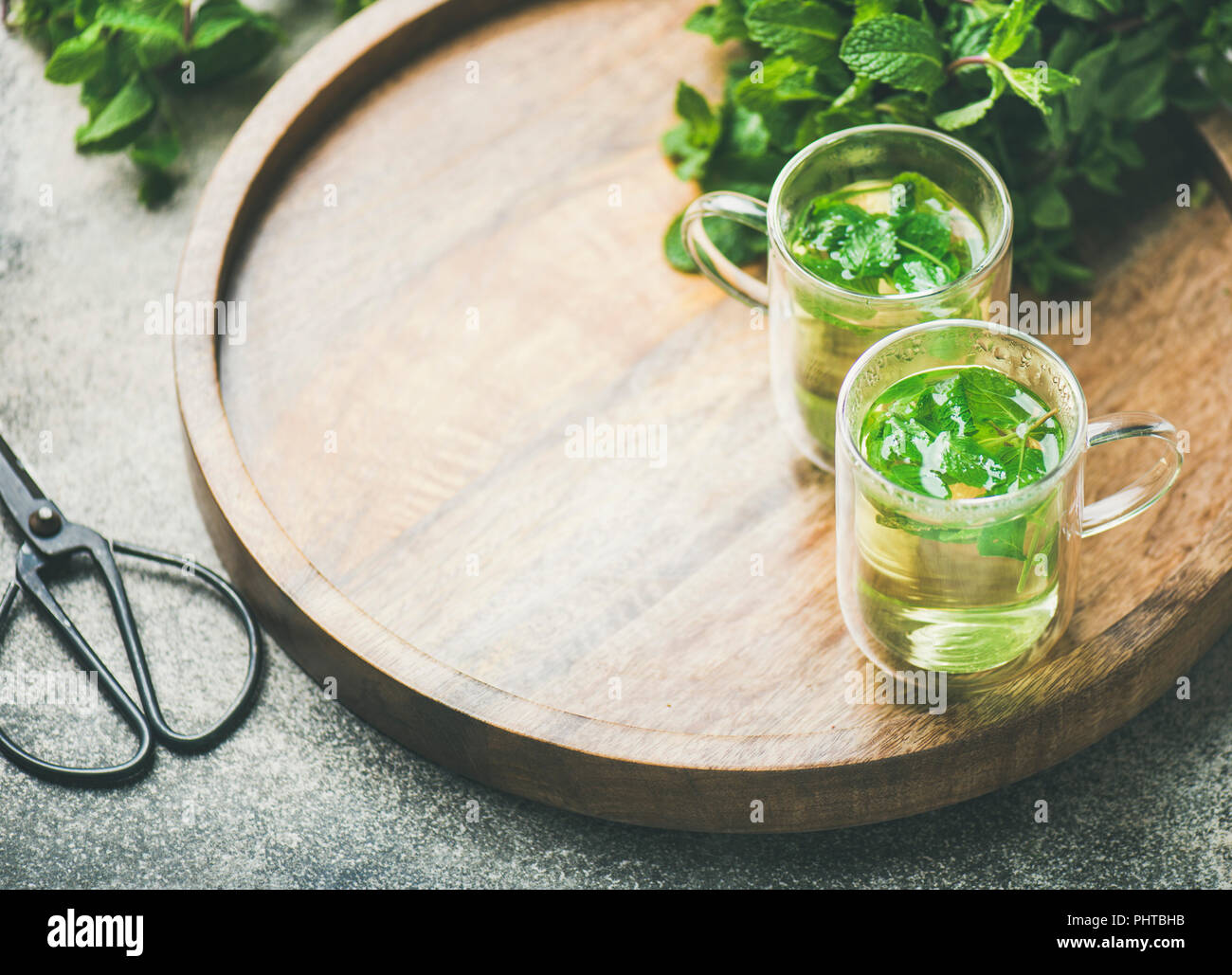 A base di erbe calde tè alla menta bevande in bicchieri di vetro sopra il vassoio in legno con fresco giardino con foglie di menta, spazio di copia Foto Stock