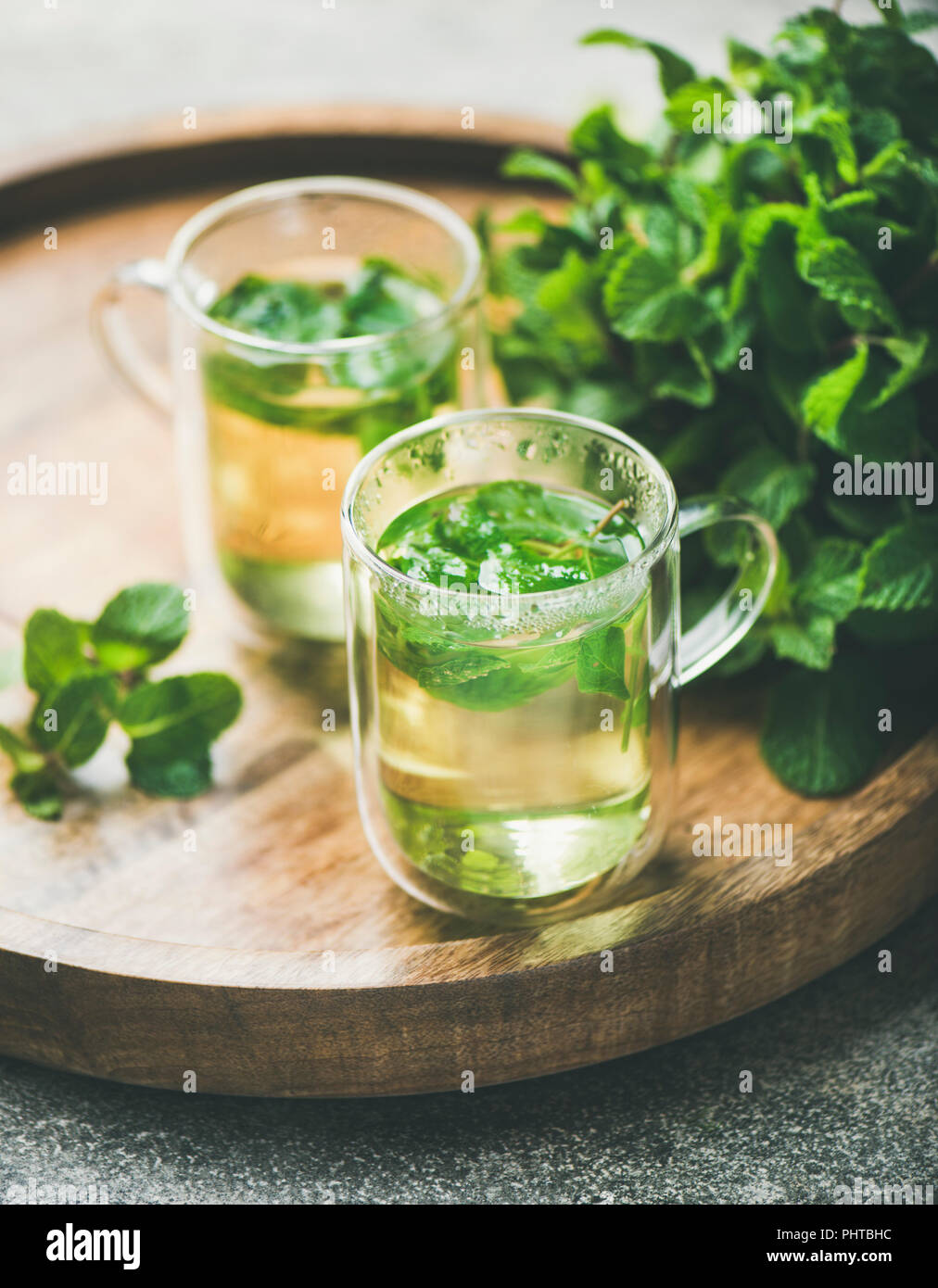 A base di erbe calde tè alla menta bevande in bicchieri di vetro sopra il vassoio in legno con fresco giardino con foglie di menta, il fuoco selettivo, close-up Foto Stock