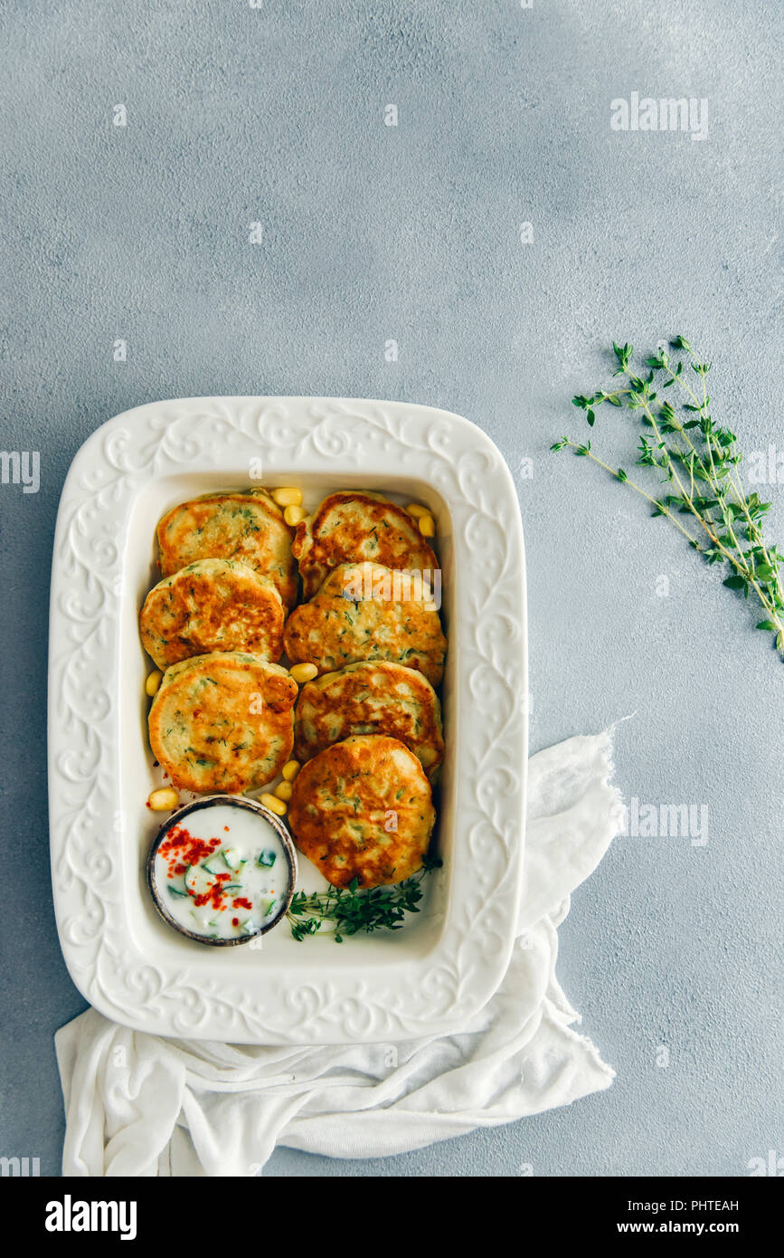 Frittelle di mais servite con salsa di yogurt e di timo fresco sul lato in una padella bianco fotografato su sfondo grigio dalla vista dall'alto. Fresco rametti di timo Foto Stock