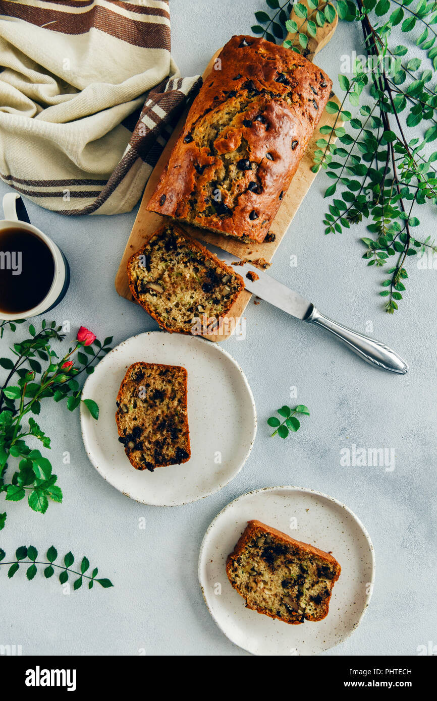 Con scaglie di cioccolato pane di zucchine con le noci tagliate a fette su un tagliere di legno e servito su due piastre di bianco accompagnato da una tazza di tè verde lascia un Foto Stock