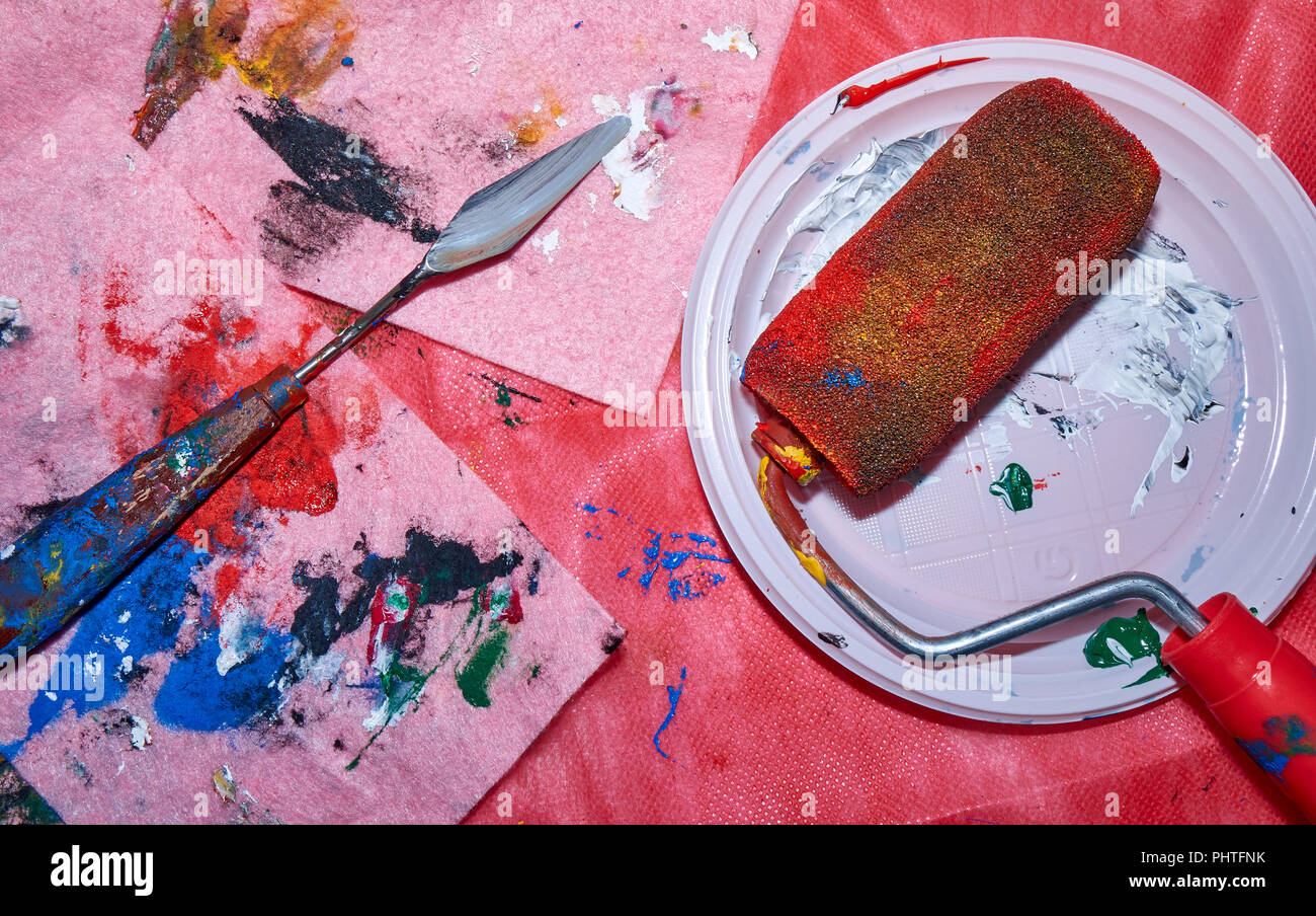 Rullo colorato giacente sulla piastra bianca con una tavolozza coltello dopo essengo utilizzato da un artista professionista per Wall arte pittura, angolo superiore, pin colorati Foto Stock