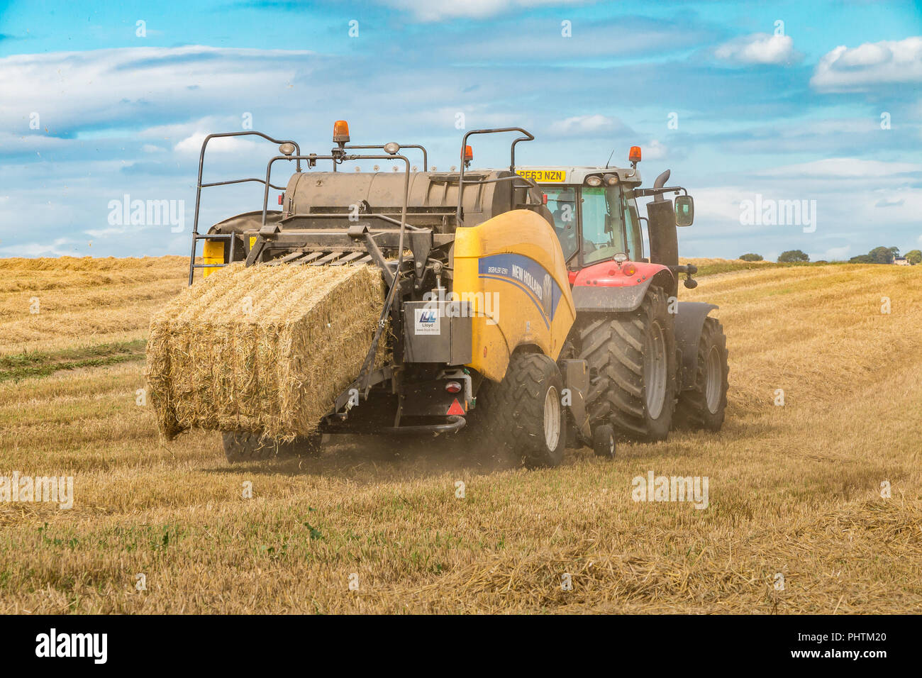 Un Massey Ferguson 7618 trattore e New Holland Bigbaler 1290 lavorando su paglia di orzo con una balla finito di essere scaricato Foto Stock