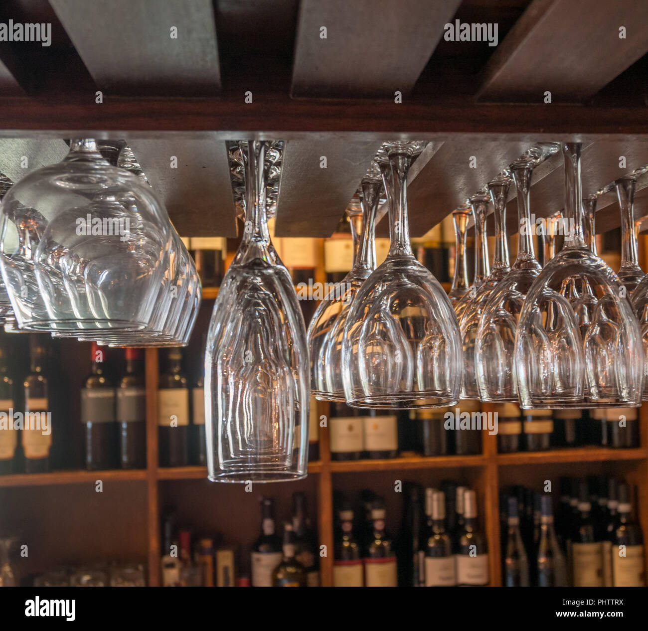 Differente tipo di occhiali appesi Fron Rack con bottiglie di vino in background Foto Stock