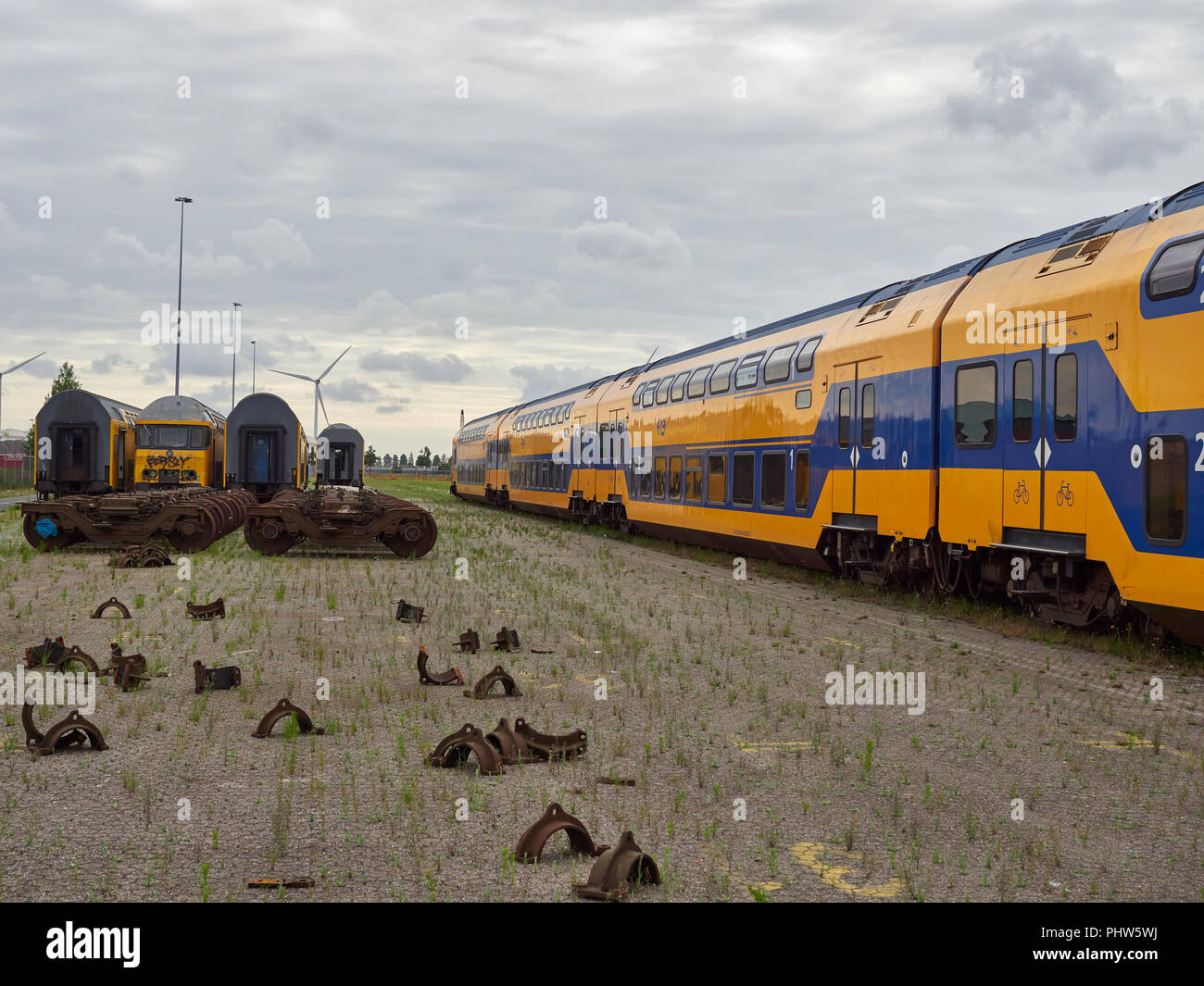 Deck a doppia stazione di carrozze passeggeri in attesa di smaltimento accanto alle righe del treno di carrelli motore e parti freno sparsi sul terreno. Holland. Foto Stock