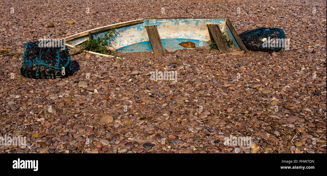 Forata la barca a remi è parzialmente sepolto in ciottoli a Sidmouth faggio in Devon England. Foto Stock