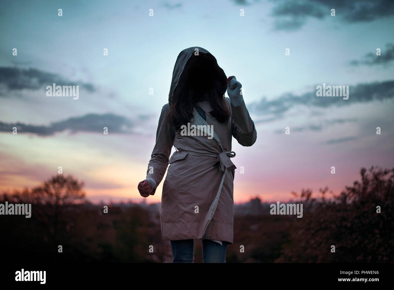 La donna non identificabili indossando incappucciati trench coat in ballo il tramonto. Misterioso, creative - Viaggi / Lifestyle concept. Londra, Regno Unito Foto Stock