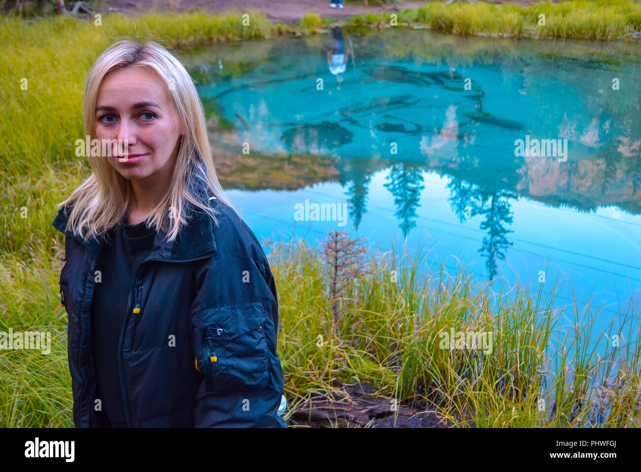 Ragazza bionda è in piedi e guardando la telecamera sullo sfondo di una pittoresca turchese del lago geyser,in cui il blu,verde,blu cerchi di salita e di Foto Stock
