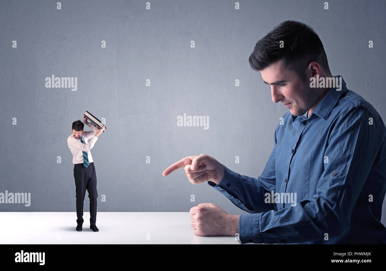 Giovane imprenditore professionale essendo arrabbiato con un altro imprenditore in miniatura nella parte anteriore di un bluastro sfondo grigio Foto Stock