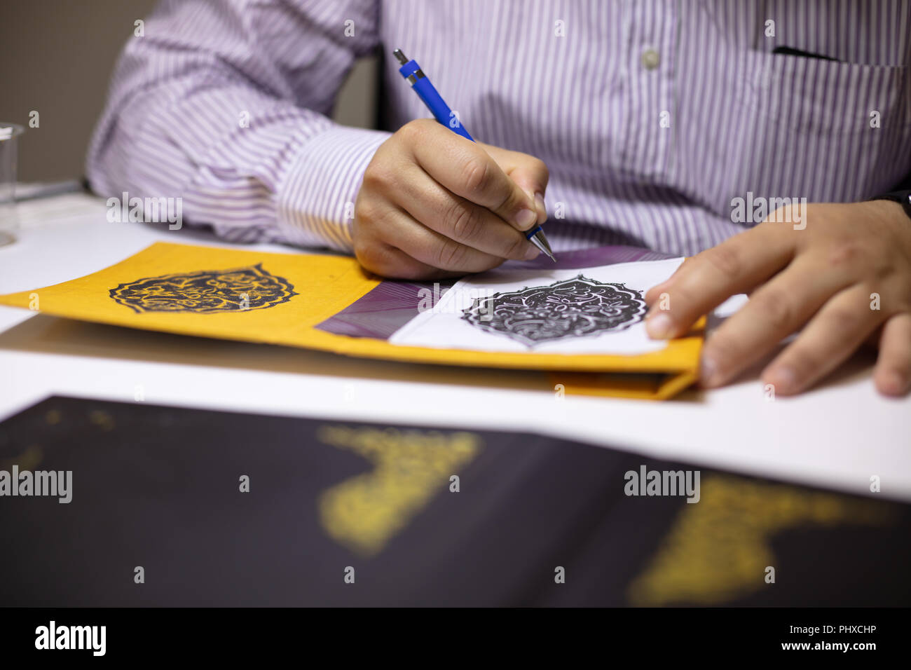 Book Binder mano che illustra le copertine del libro nel suo laboratorio modelli calligrafico al suo tavolo di lavoro in una vista ravvicinata Foto Stock