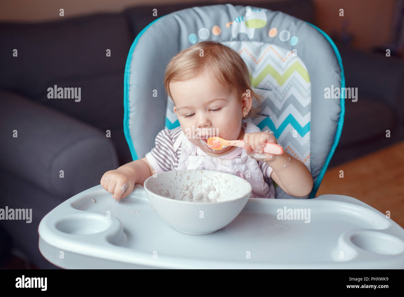 Ritratto di carino adorabile bambino caucasico kid ragazza seduta nel seggiolone mangiare cereali con cucchiaio. Lo stile di vita di tutti i giorni. Candide vero e autentico momento Foto Stock