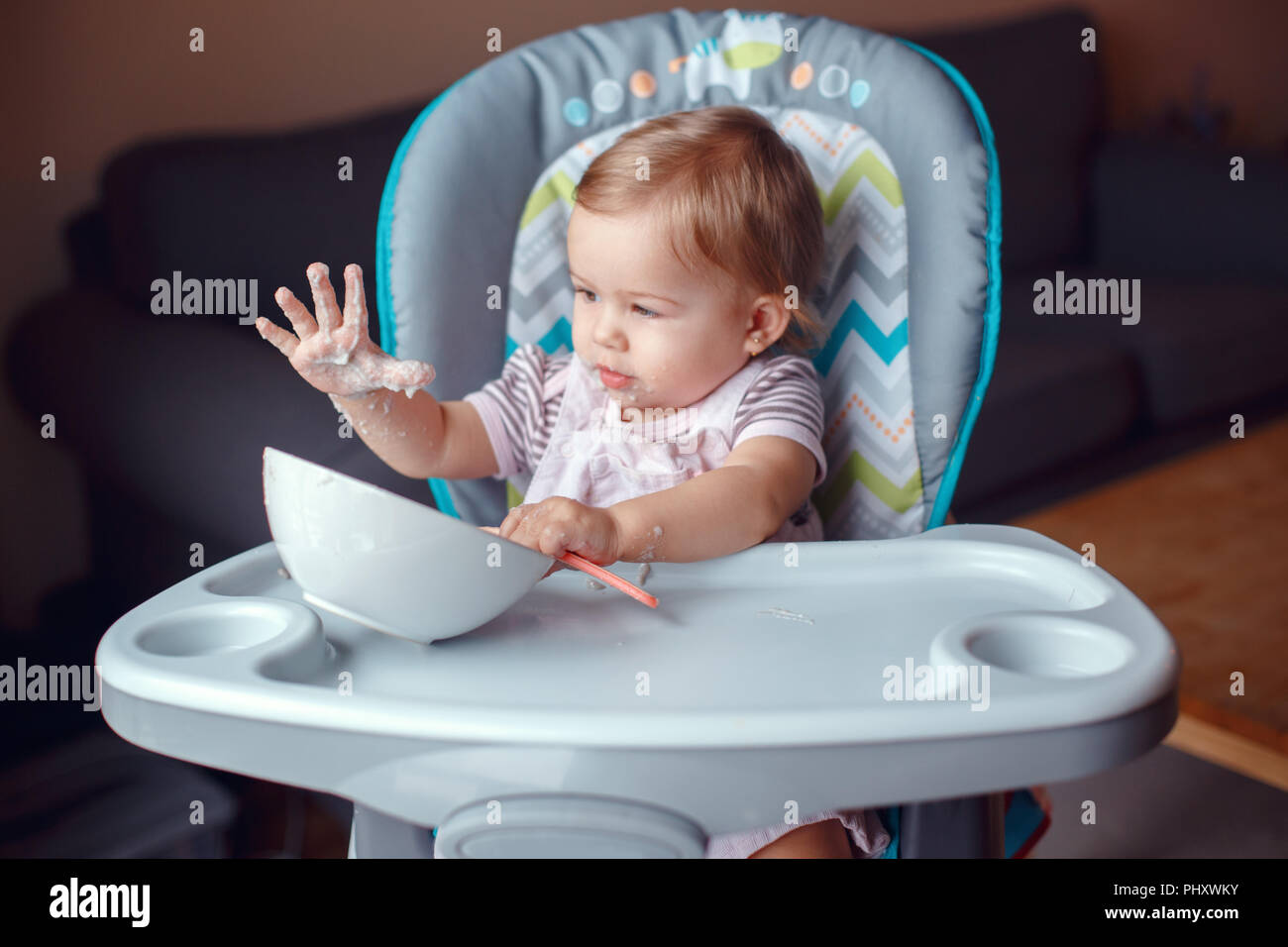 Ritratto di carino adorabile bambino caucasico kid ragazza seduta nel seggiolone mangiare cereali con cucchiaio. Lo stile di vita di tutti i giorni. Candide vero e autentico momento Foto Stock