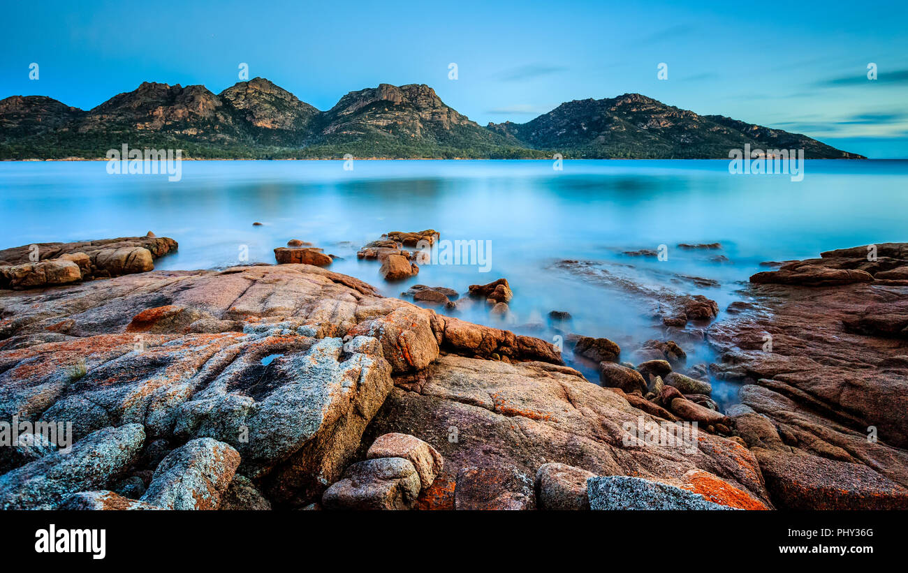 I pericoli nel Parco Nazionale di Freycinet al tramonto, visto dal Coles Bay in Tasmania, Australia, con lichene arancione su rocce di granito in primo piano. Foto Stock