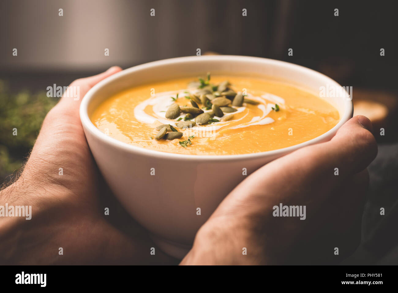 Ciotola di calda zuppa di zucca in mani. Recipiente di contenimento del vegan zuppa di zucca. Comfort food. Immagine dai toni, il fuoco selettivo Foto Stock