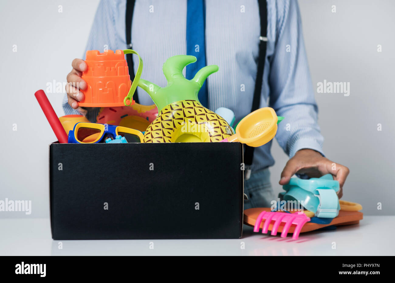 Primo piano di un uomo caucasico, alla sua scrivania da ufficio, tenendo fuori o memorizzazione in una scatola alcuni estate roba, come giocattolo diverse pale, rastrelli e secchi, Foto Stock