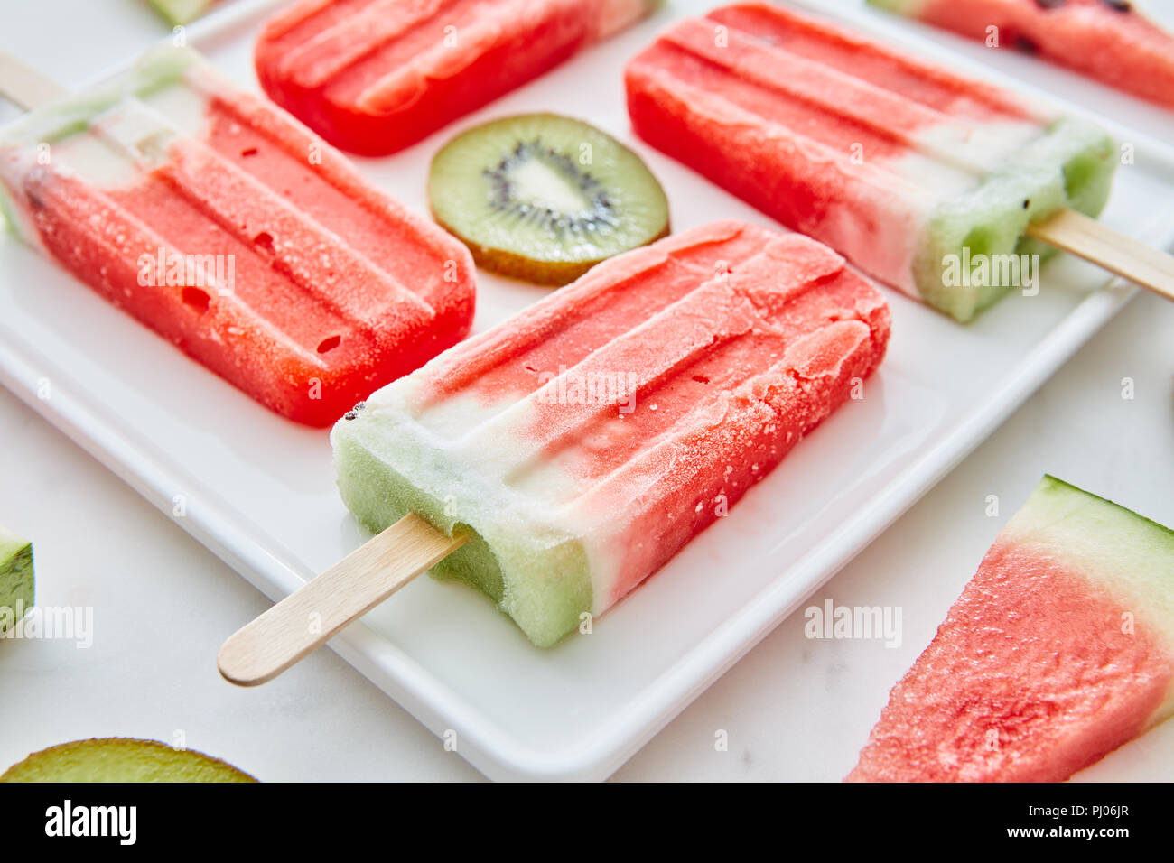 Close-up di un multicolore frutti congelati i frullati con pezzi rotondi di kiwi e pezzi triangolari di anguria in una piastra bianca su un marmo grigio Sfondo.dietetiche dessert estivo Foto Stock