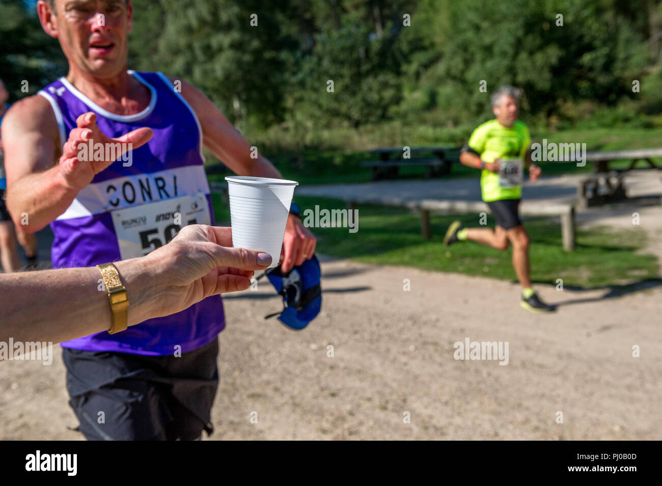 I corridori di afferrare un bicchiere di plastica di acqua durante la 10k l'esecuzione. Foto Stock