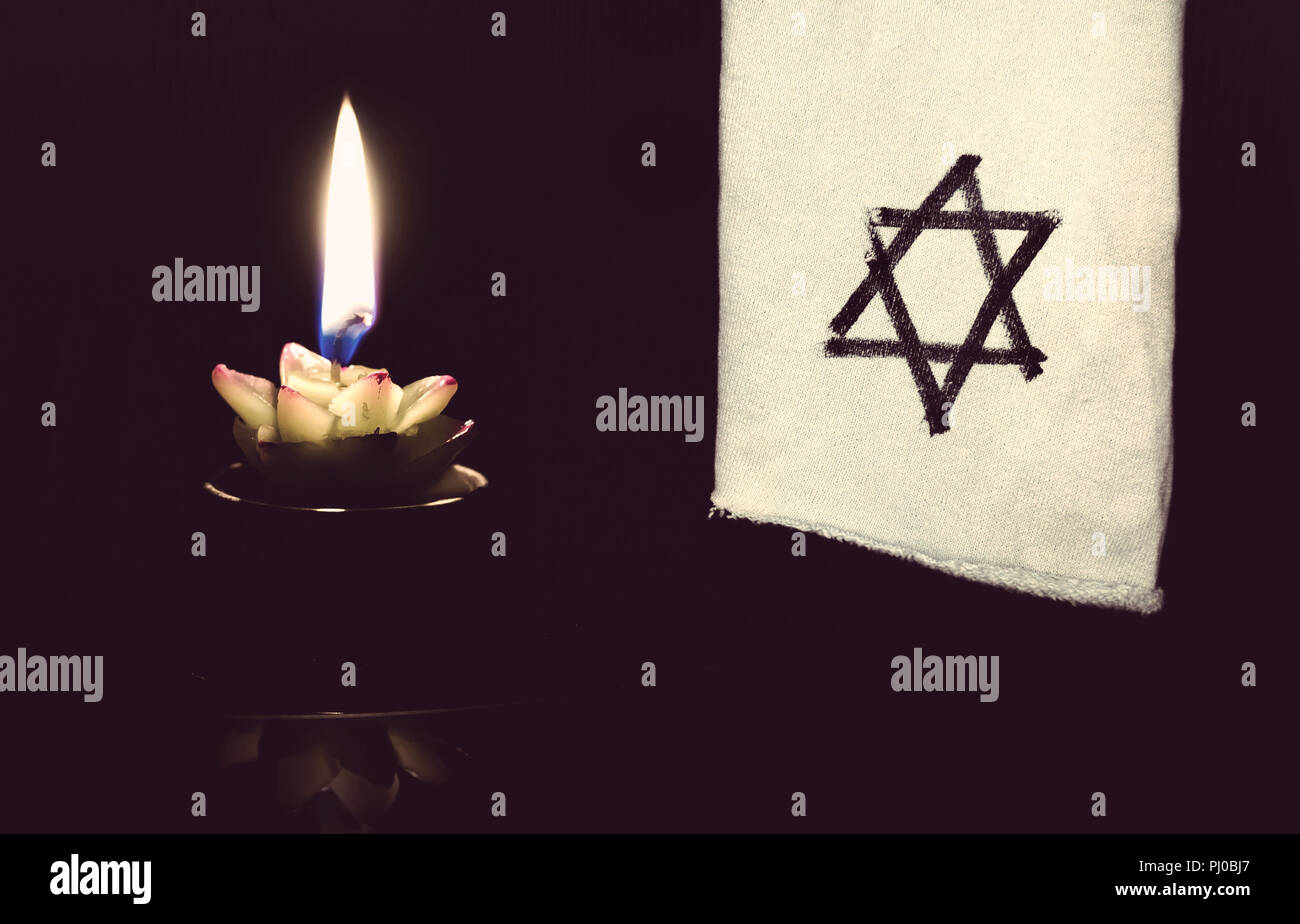 La stella di Davide e la candela si erge sulla tavola su uno sfondo nero in memoria delle vittime dell'Olocausto e il genocidio. Foto Stock