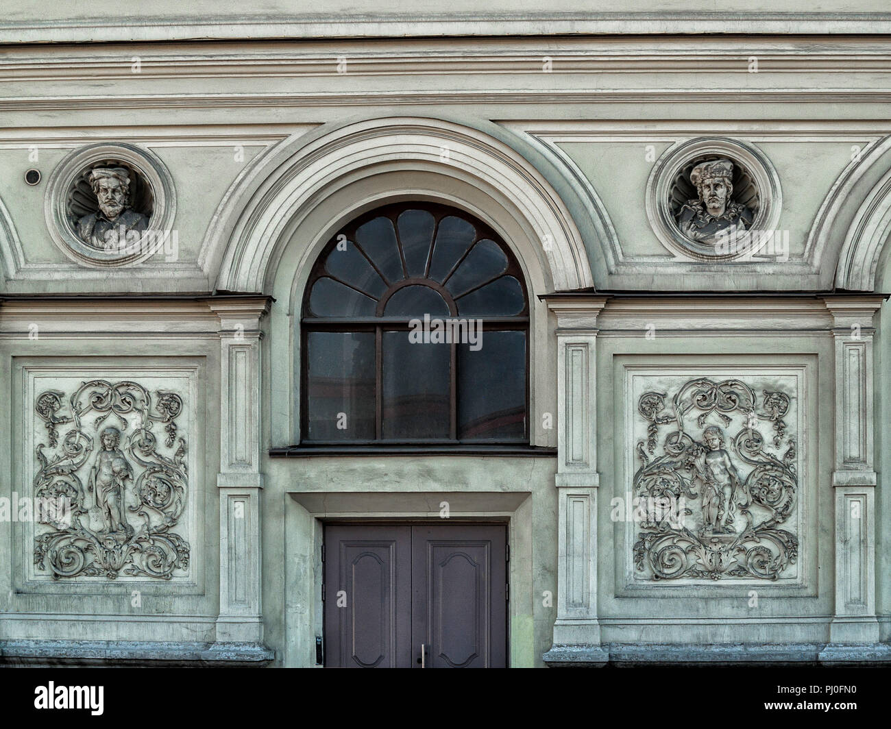 Sulla facciata del palazzo nella città di San Pietroburgo è un giro di finestra ad arco con vetro scuro, due bassorilievi con ritratti, un riquadro di scultura Foto Stock